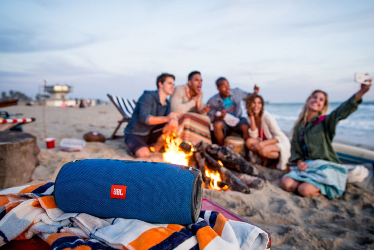 Friends beside a bonfire on the beach with the JBL portable speaker