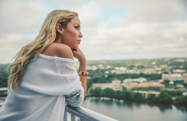 A woman standing on a balcony and
looking over a lake while wearing a wisewear activity tracker.